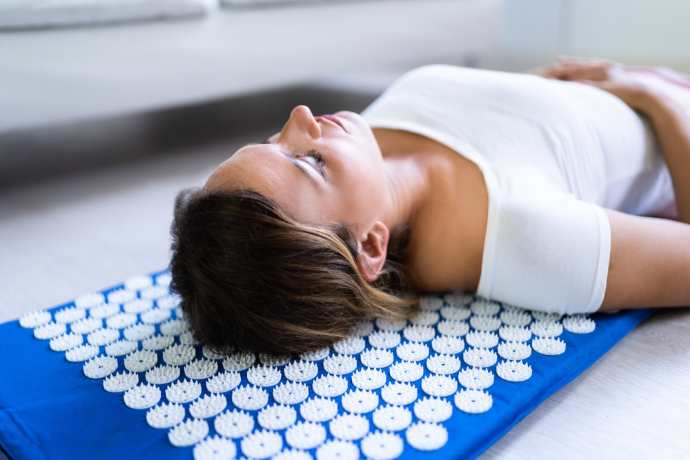 A woman lying on a acupressure mat with her head on the floor, practicing a yoga pose.
