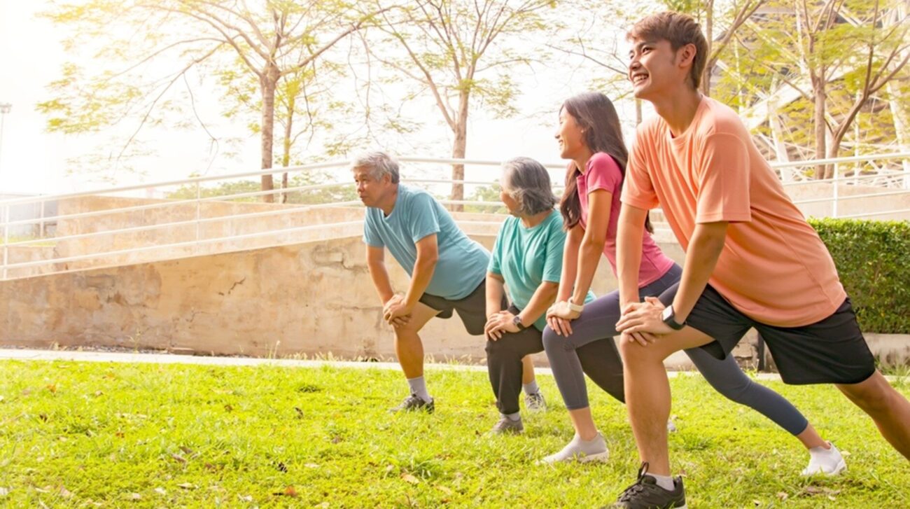 Asian family exercising in park parents and children stretching and jogging together, enjoying outdoor fitness.