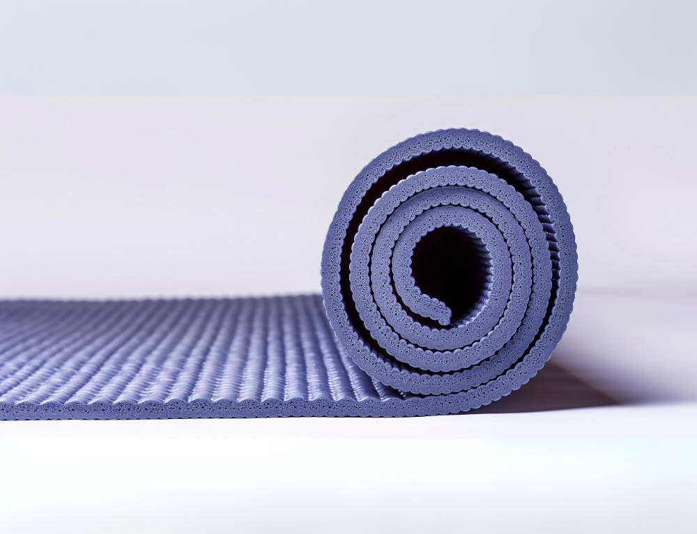 A close-up of a single yoga mat unrolled on the floor, highlighting its thickness and cushioning with a focus on texture and material.