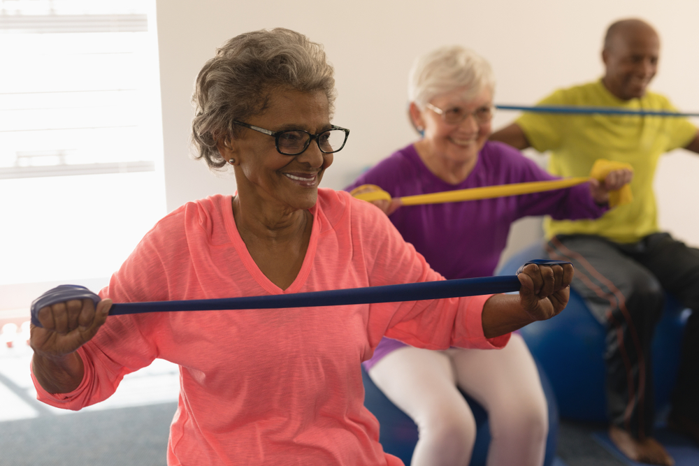 Front view of happy diverse senior woman exercising with resistance band in fitness studio