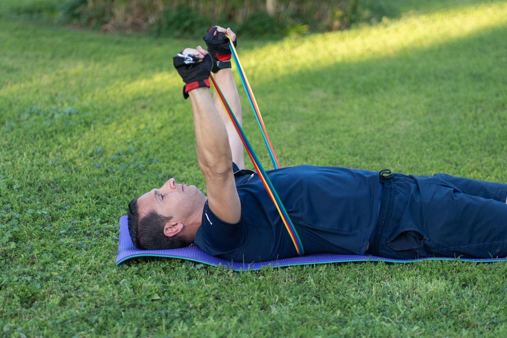 Man lying on a mat doing chest presses with resistance bands.