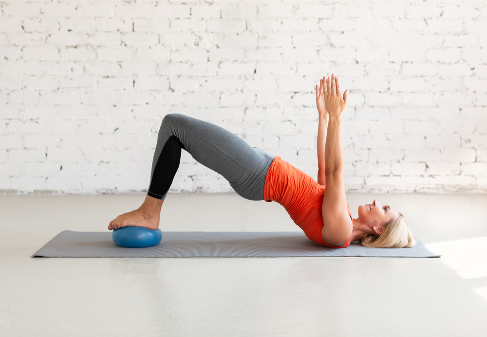 Pilates with small fit ball. Caucasian woman practice gluteal bridge balance on a mat, in loft white studio indoor, selective focus. Workout, fitness, coach, healthy lifestyle concept.