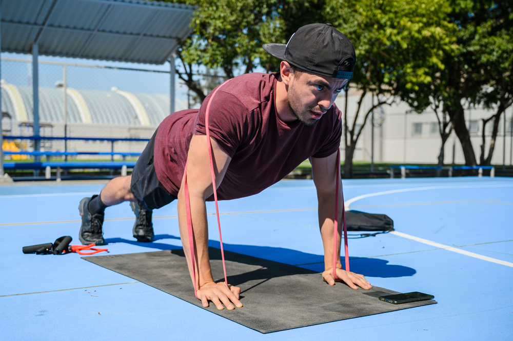 hispanic male athlete trainer working out with resistance bands, push ups and body weight training. Latin man training at a park on a sunny day for well beign