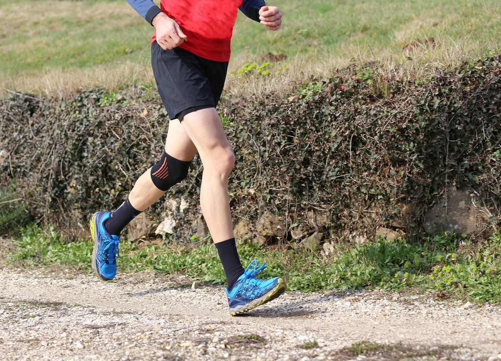 man runner during the cross-country race with his knee wrapped by a knee brace