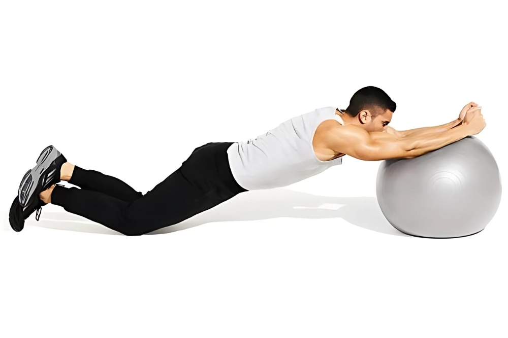 young sporty man doing plank with legs on fitball at gym