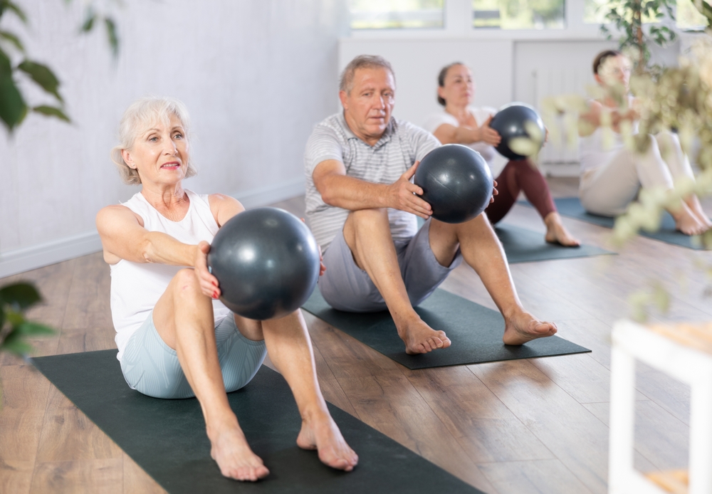 Portrait of mature people doing exercises for press with pilates ball during group class in fitness studio