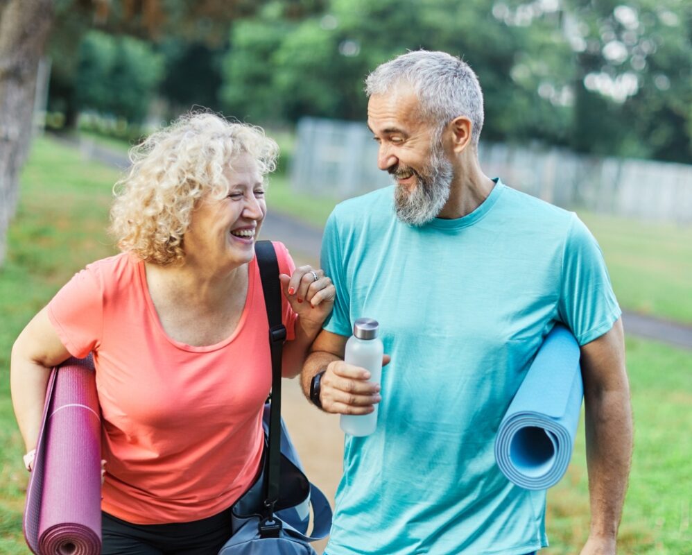 Happy active middle aged couple having fun talking and bonding after having a yoga pilates exercise in park outdoors